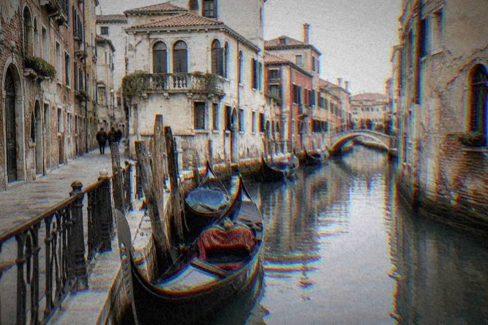 A gondola moored beside a narrow Venetian canal with tall brick buildings