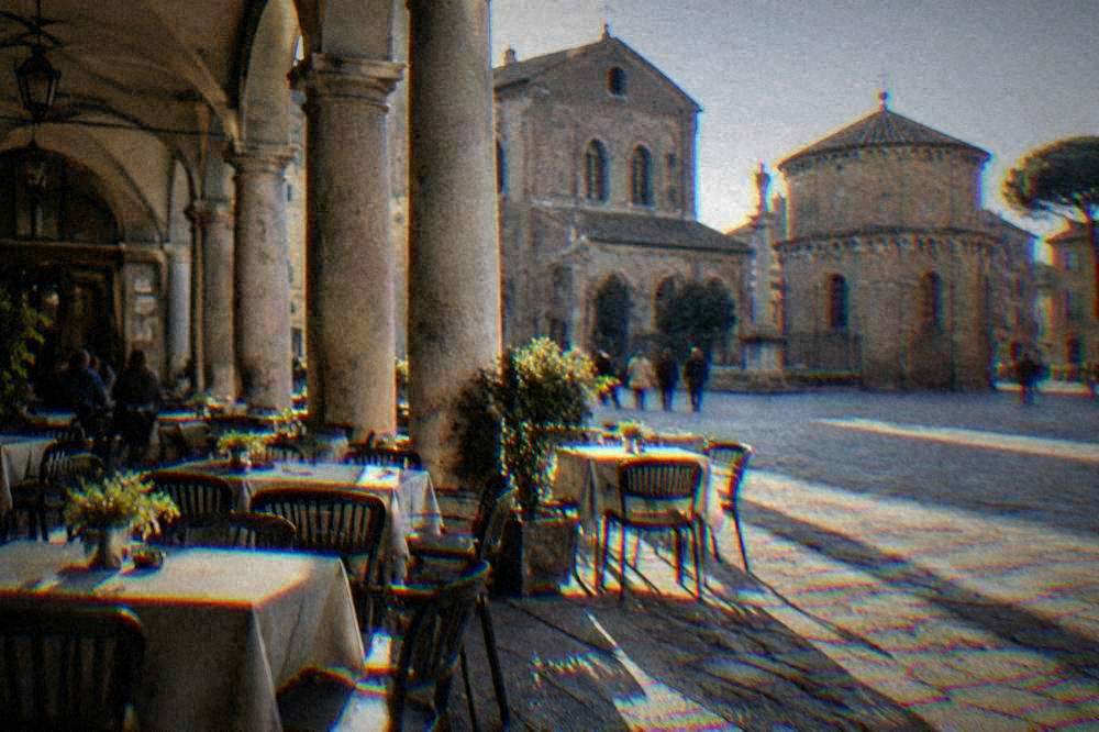Morning light on a Ravenna piazza with cafe tables set out under arcades