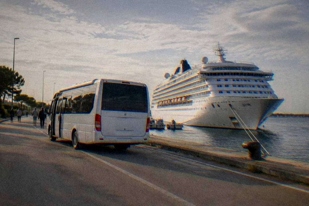A shuttle bus parked on a waterfront road beside a moored cruise ship