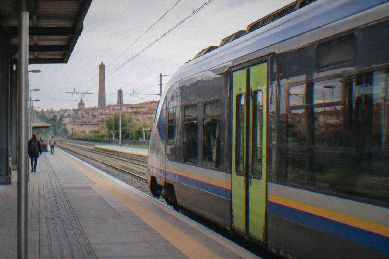 A regional train waiting at an Italian railway station platform beside a historic brick station building