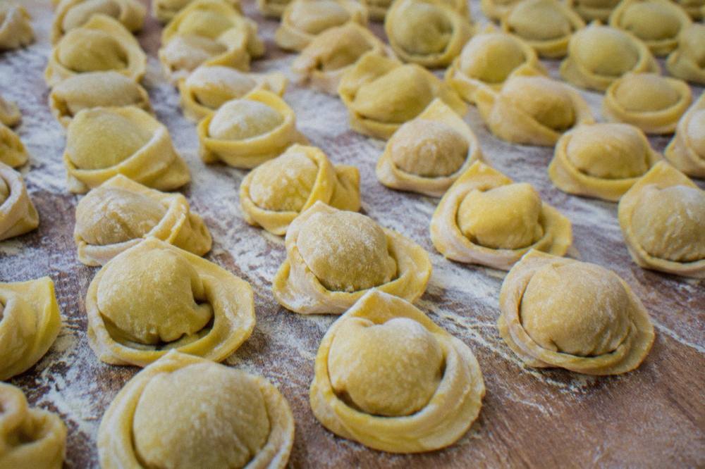 Uncooked cappelletti arranged in rows on a floured wooden board