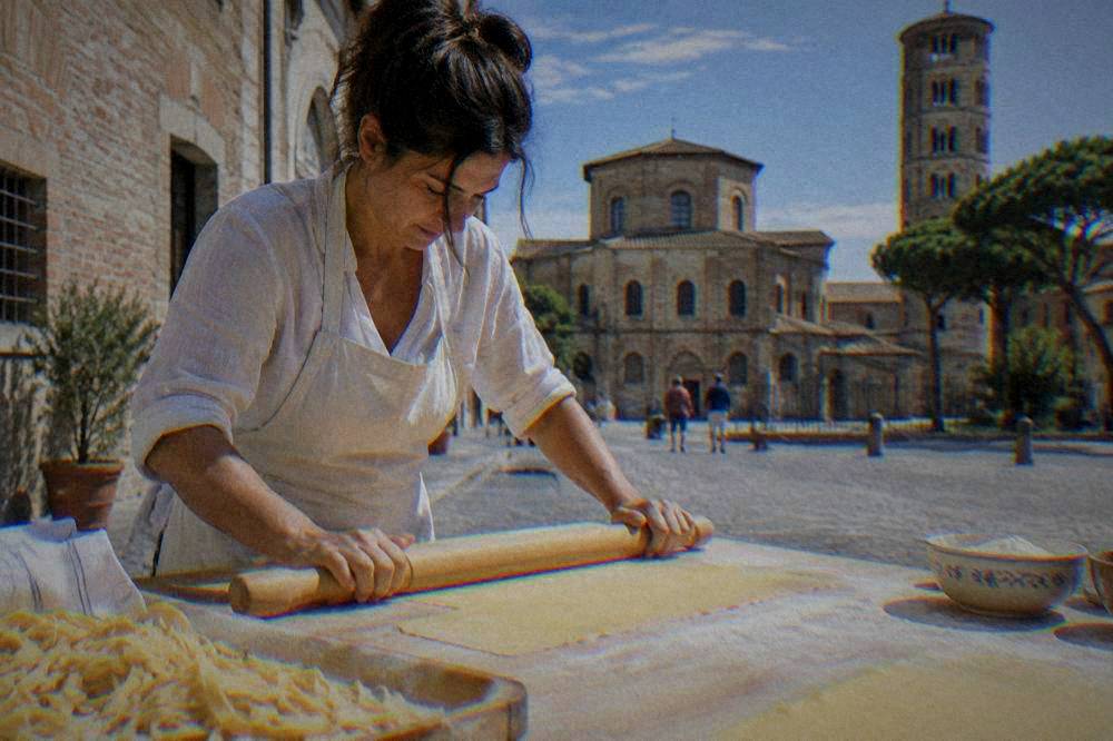 A cook rolling thin sheets of egg pasta dough with a wooden rolling pin