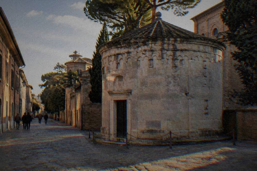 The small stone exterior of Dante's tomb in Ravenna with a narrow street beside it