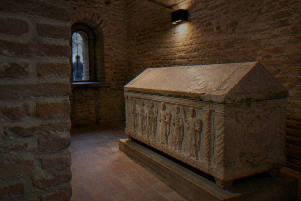 A stone sarcophagus in a small brick chamber lit by a lamp