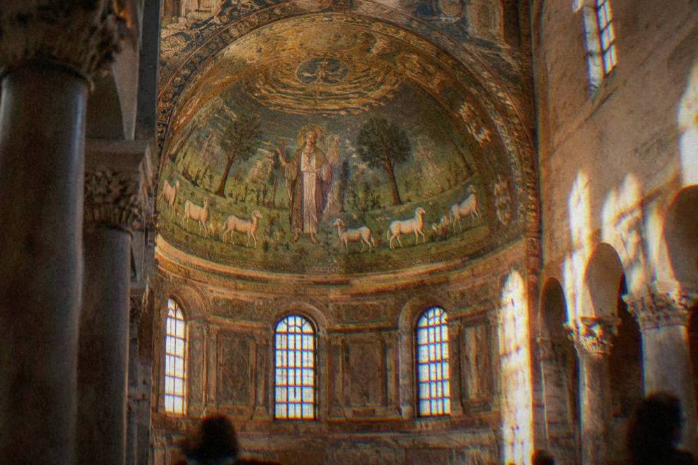 Basilica apse mosaic of a green landscape with sheep and a saintly figure