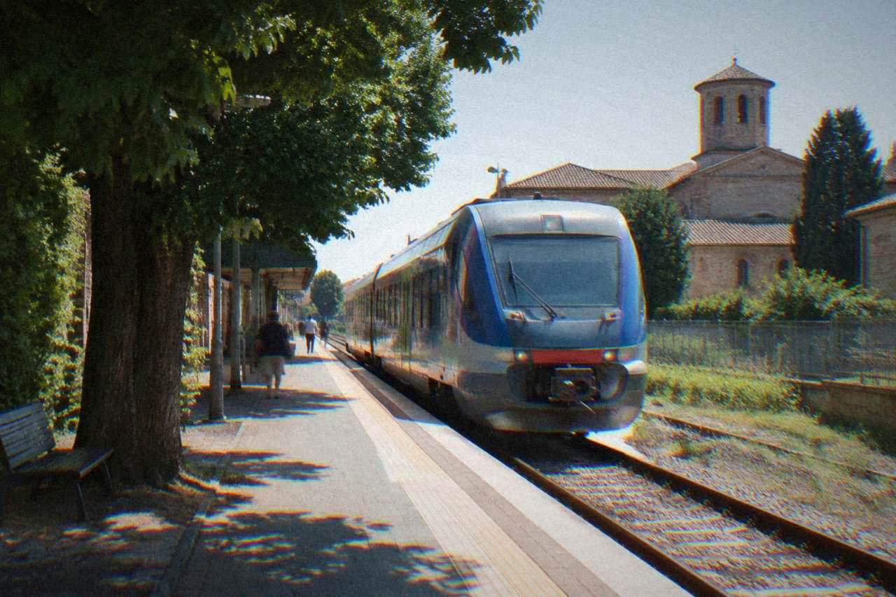 A regional train at a small Italian railway station platform in the morning light