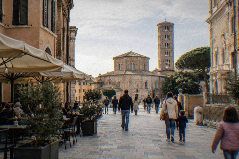 Families and visitors walking on a wide pedestrian street in Ravenna near cafe tables