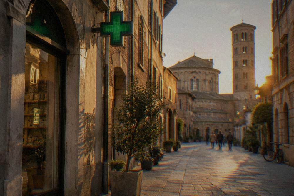 A green pharmacy cross sign above a shopfront on an Italian street