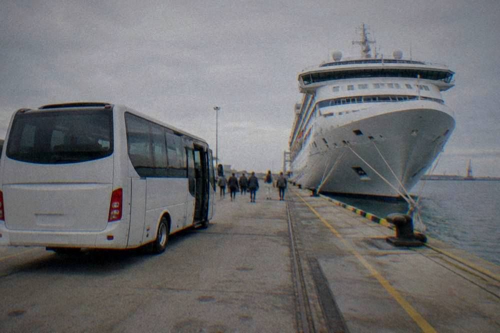 A shuttle bus parked at a cruise terminal quay beside a moored ship