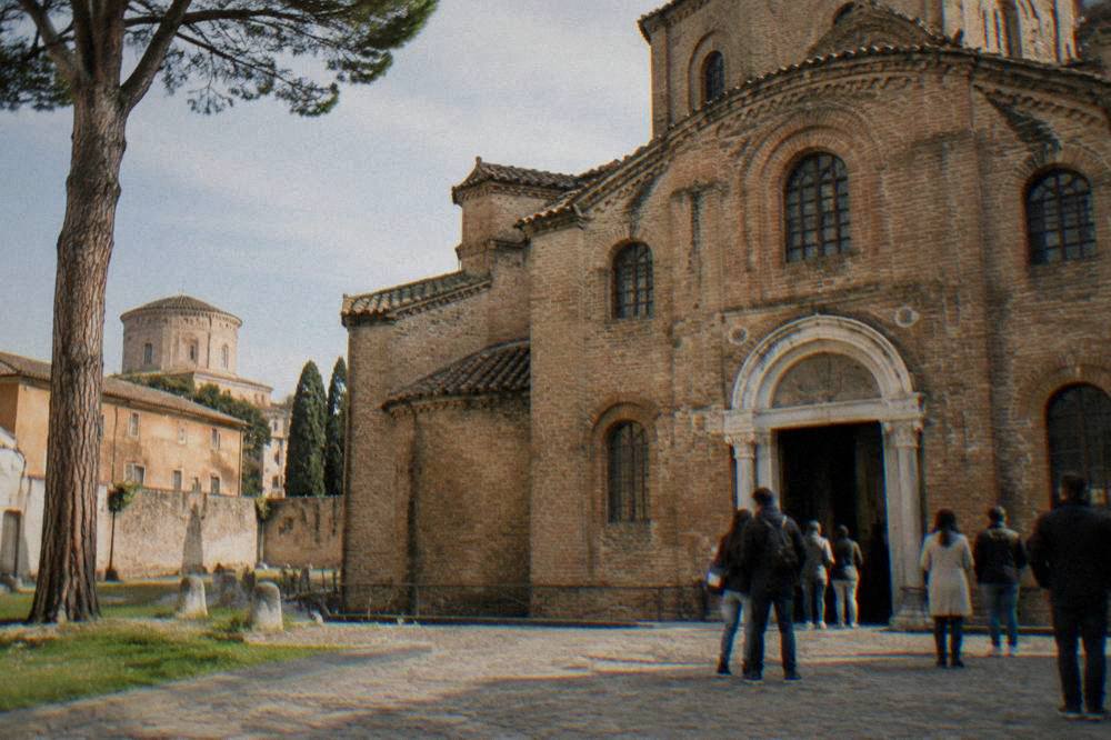 Visitors in a short queue at the entrance of a brick Byzantine church in Ravenna