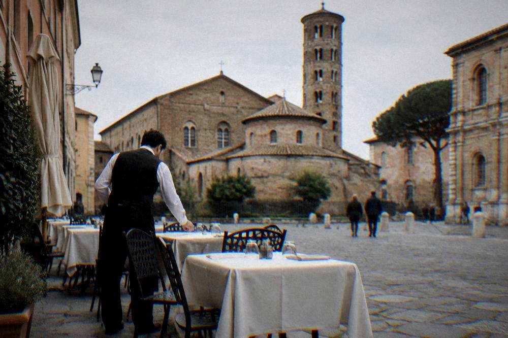 A waiter setting tables outside a small restaurant on a Ravenna square