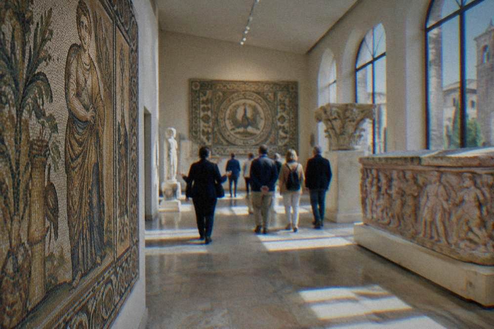 Travellers walking with a guide through a bright museum gallery of ancient stone and mosaic