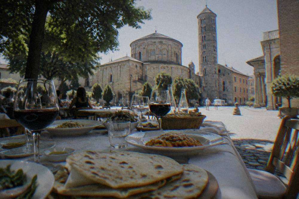 A long table with fresh piadina bread, pasta dishes and glasses of wine at an outdoor lunch