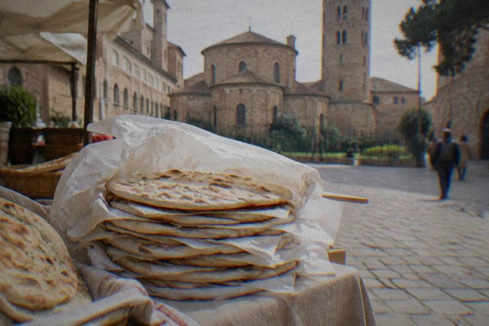 A folded flatbread in paper held in one hand beside a narrow Italian street
