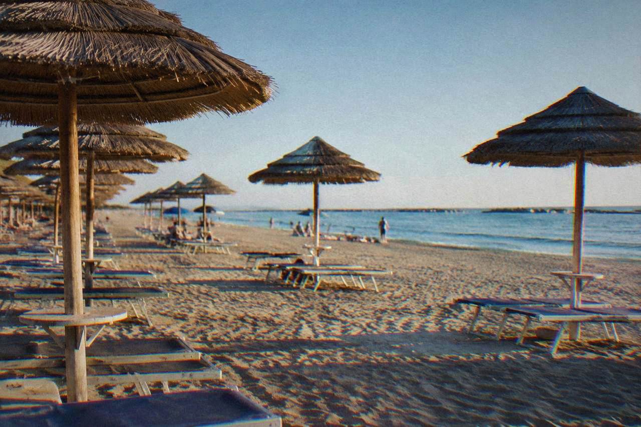 Rows of sun umbrellas standing on a wide sandy Adriatic beach beside a wooden walkway