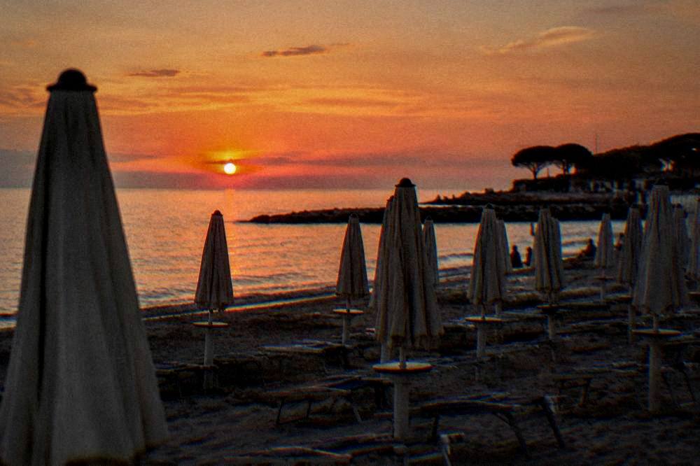 Empty beach umbrellas stacked at the edge of a resort as evening light falls on the sand
