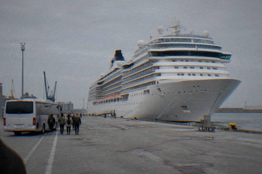 Cruise ship docked at an industrial port terminal with a shuttle bus waiting nearby