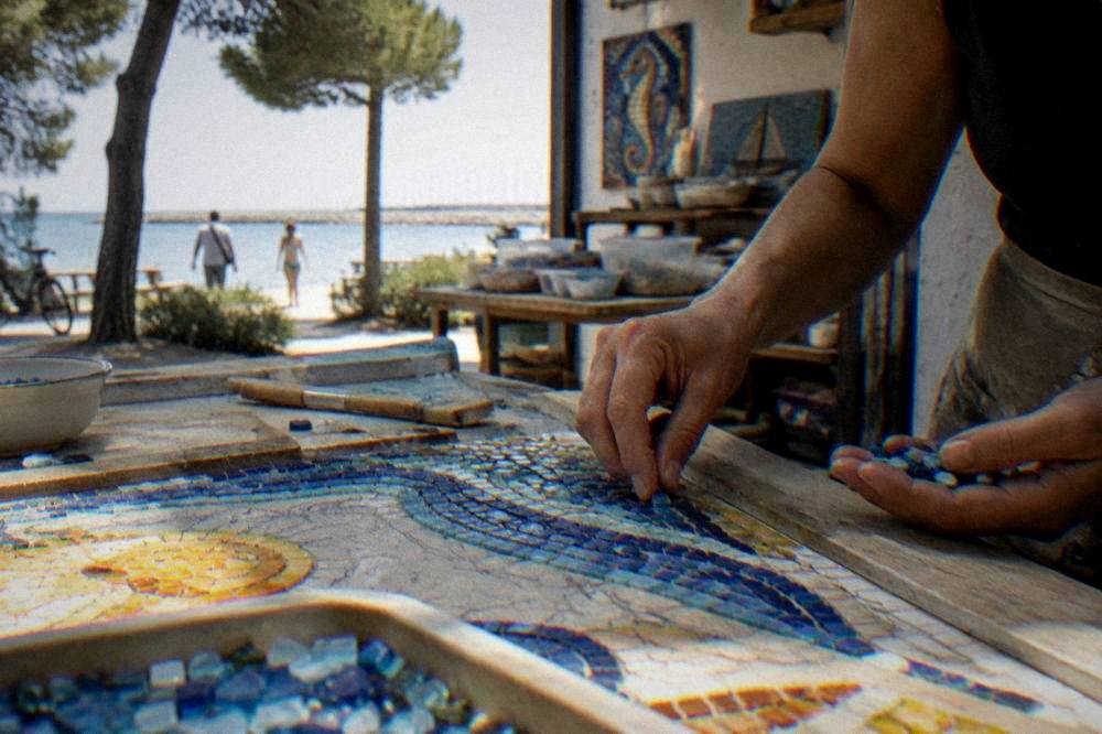 Artisan hands placing small glass tiles into a mosaic on a workbench in a workshop
