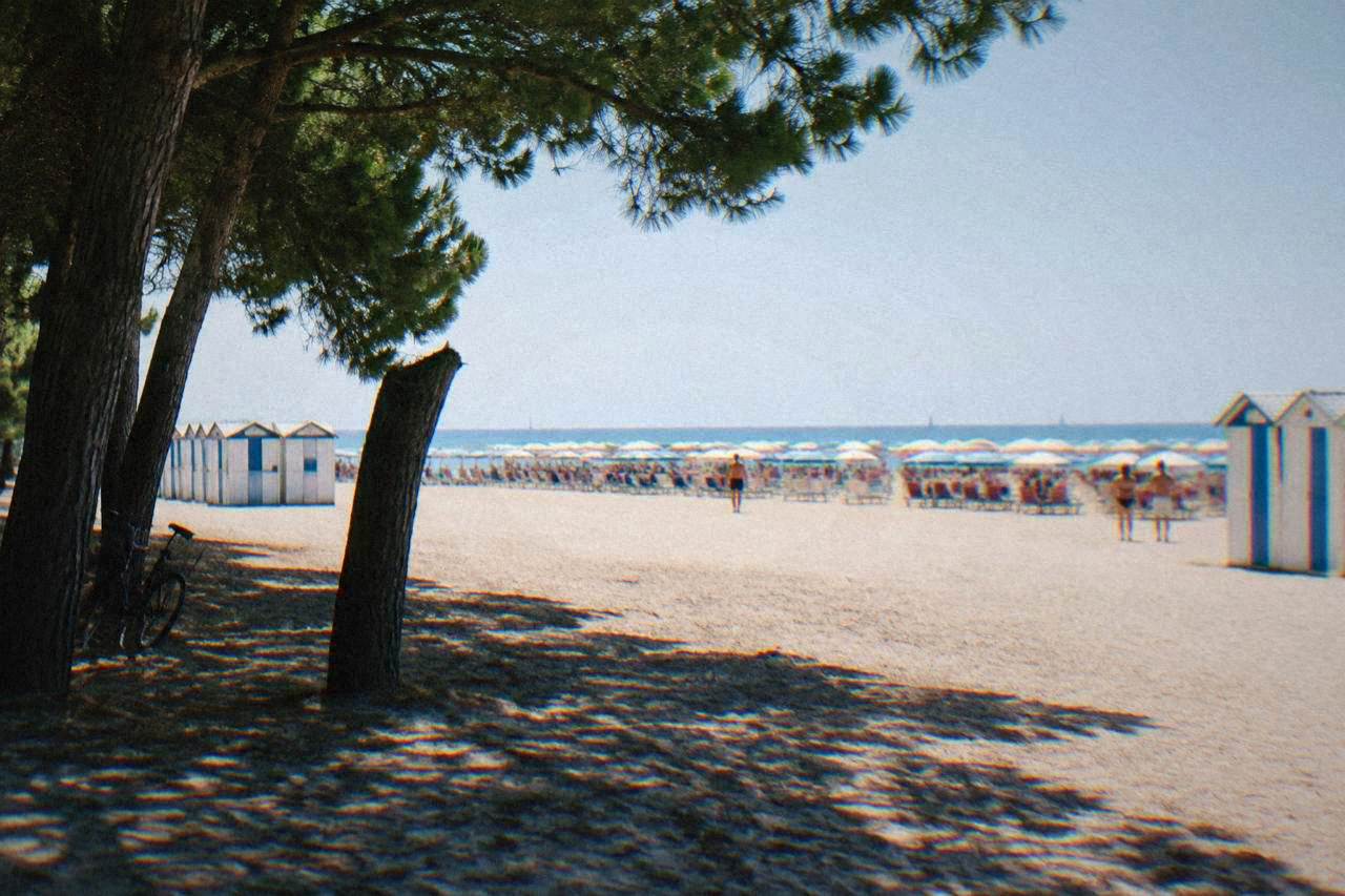 Wide sandy Adriatic beach with rows of umbrellas and bathing cabins under a clear sky