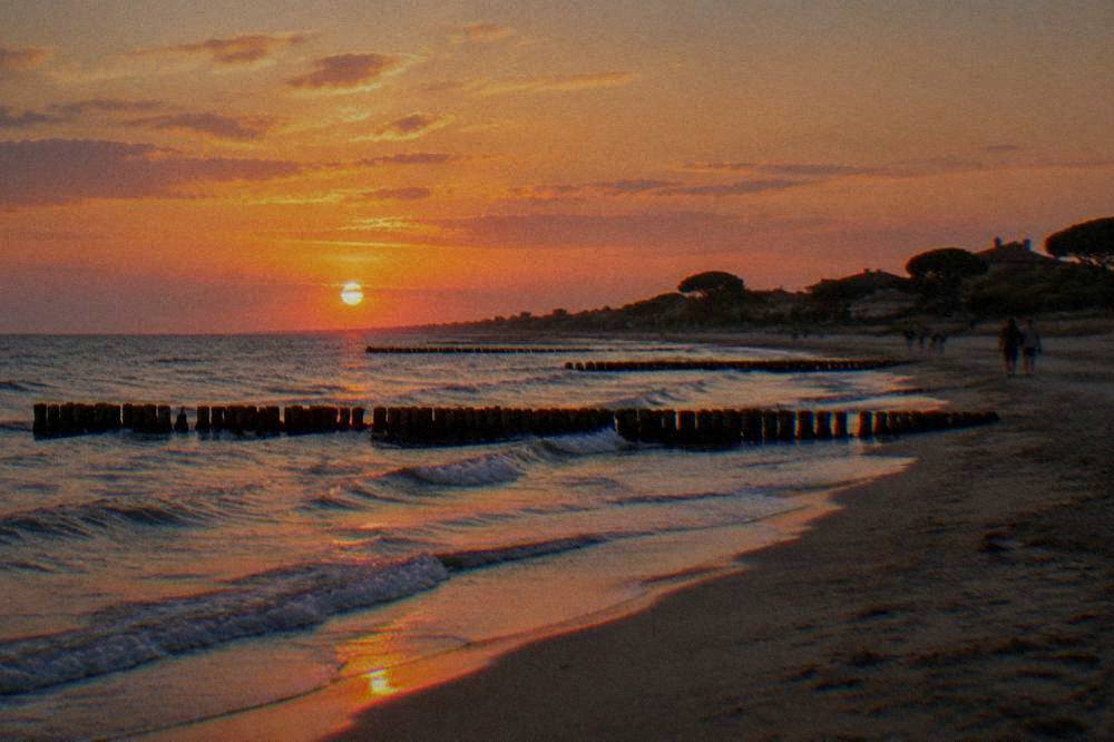 Sunset over the Adriatic seen from a sandy beach with wooden groynes