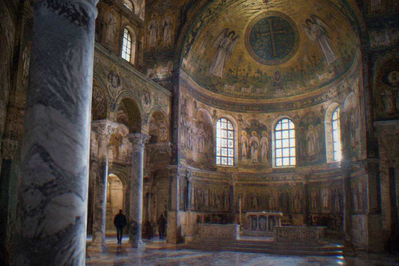 Golden mosaic interior of an early Christian church in Ravenna with marble columns and a domed ceiling