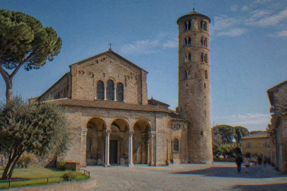 Exterior of a brick basilica in Ravenna with a simple round bell tower under a blue sky