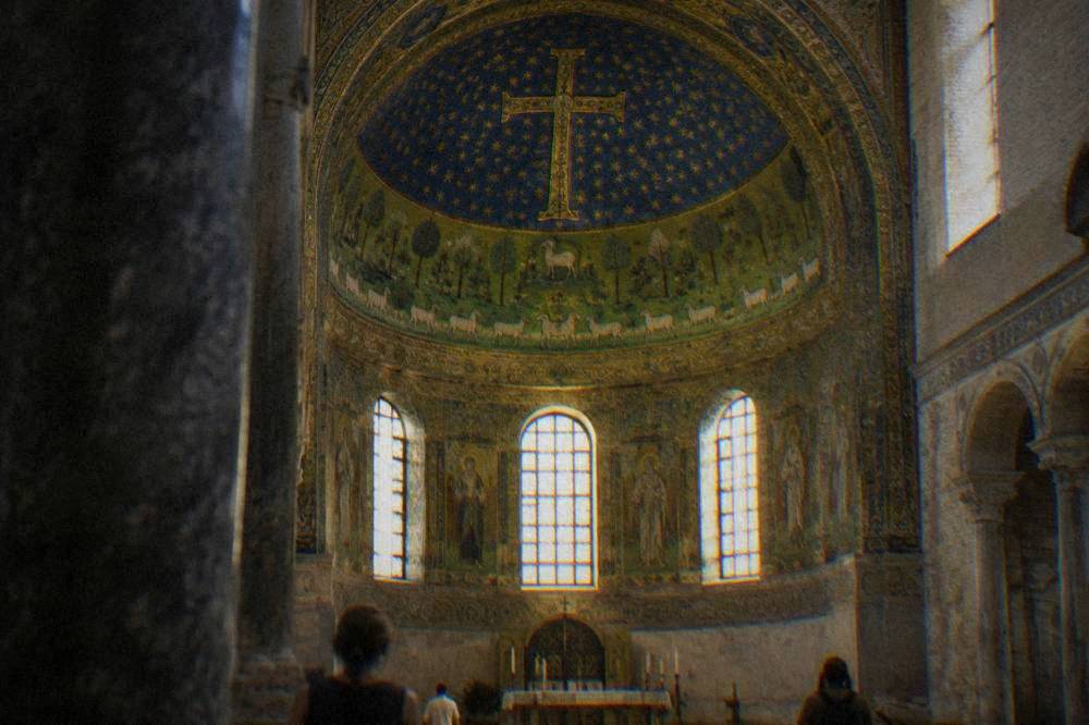 Interior of a church apse with a green meadow mosaic and sheep beneath a starry gold cross