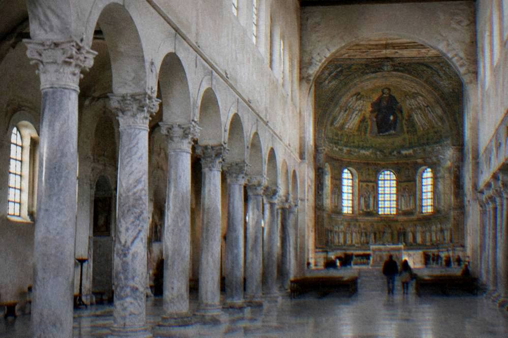 Tall pale basilica interior with marble columns and a distant mosaic apse