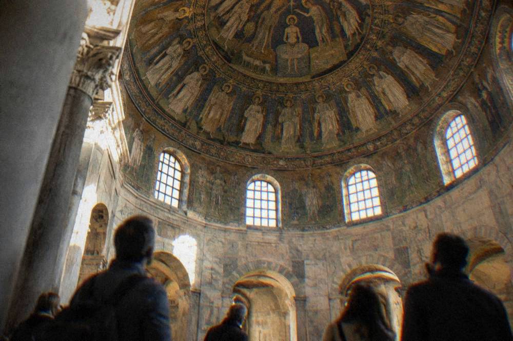 Visitors standing beneath the dome of a baptistery in Ravenna looking up at mosaic decoration