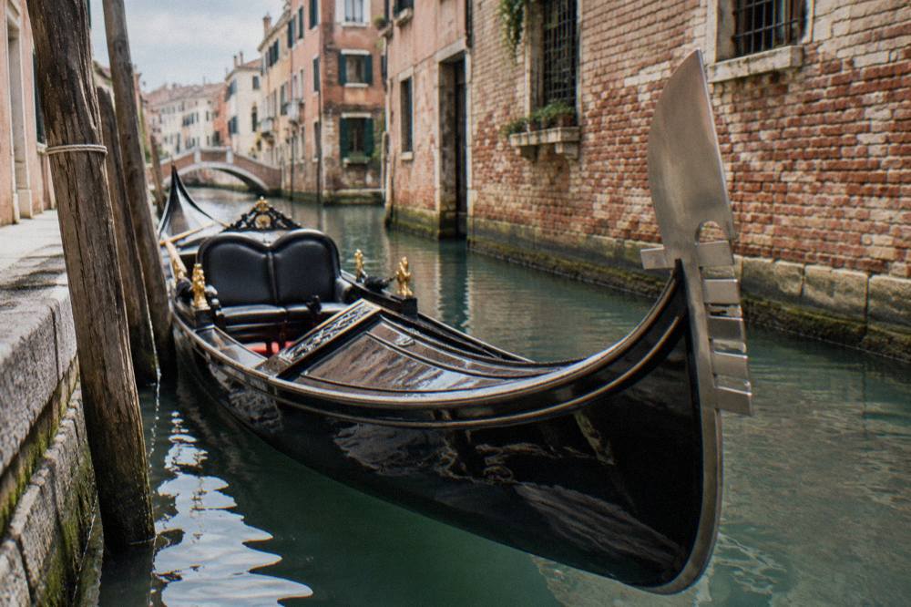 A gondolier steering a wooden gondola along a narrow canal lined with old brick buildings