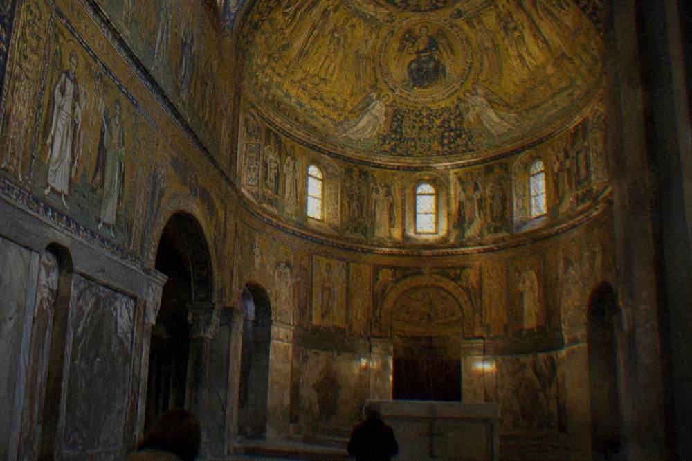 A dim chapel interior lit by golden mosaic decoration covering the dome and walls
