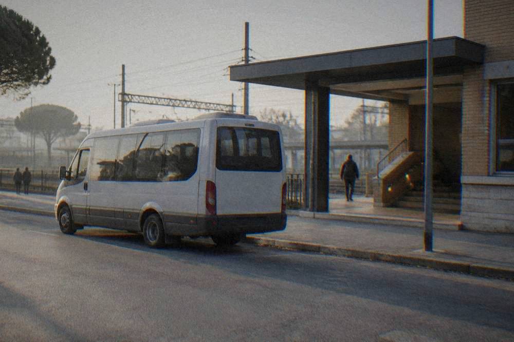 A small shuttle bus parked on a street beside a railway station entrance