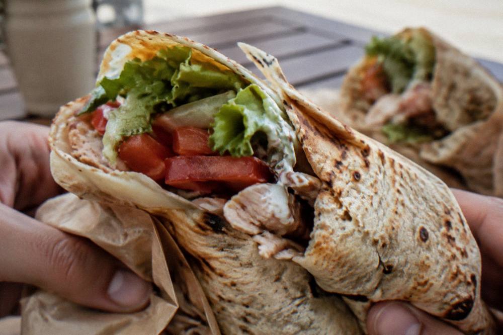 Two people sharing a flatbread wrap at an outdoor table on a quiet old street
