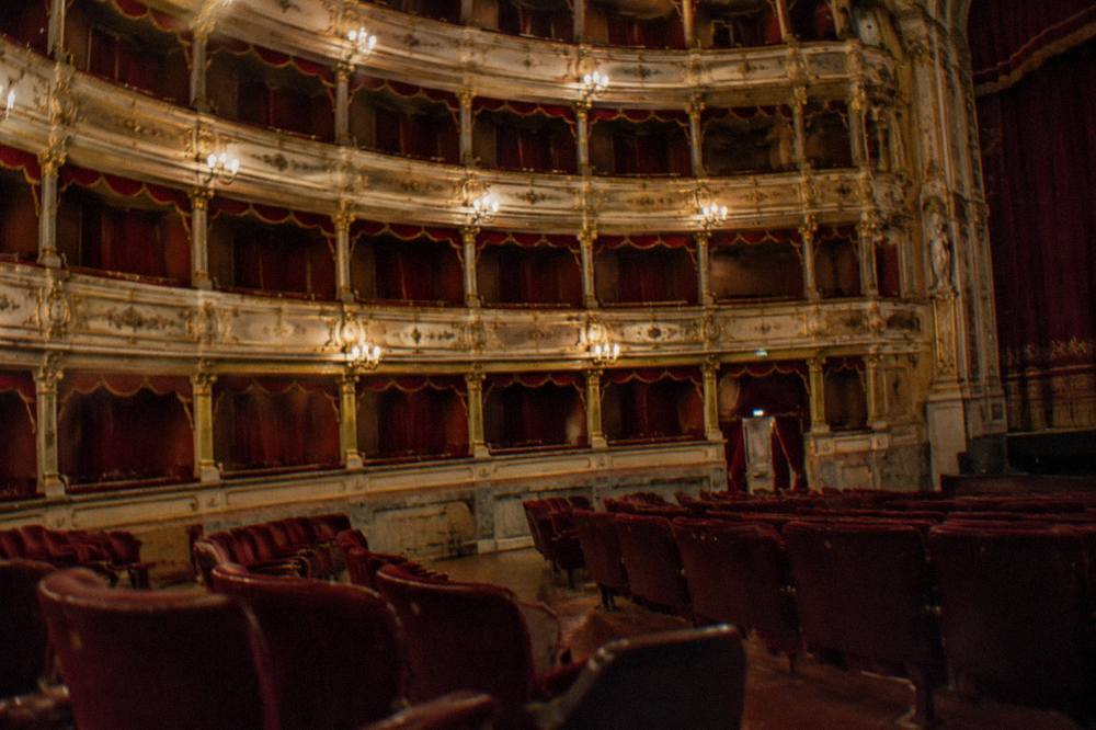 A gilded theatre auditorium with red seating and ornate balconies lit for an evening performance
