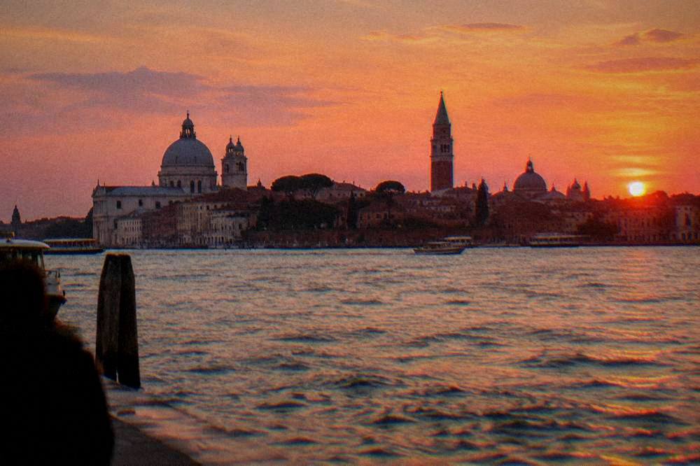 An evening view of a canal city skyline with domes and a campanile across open water
