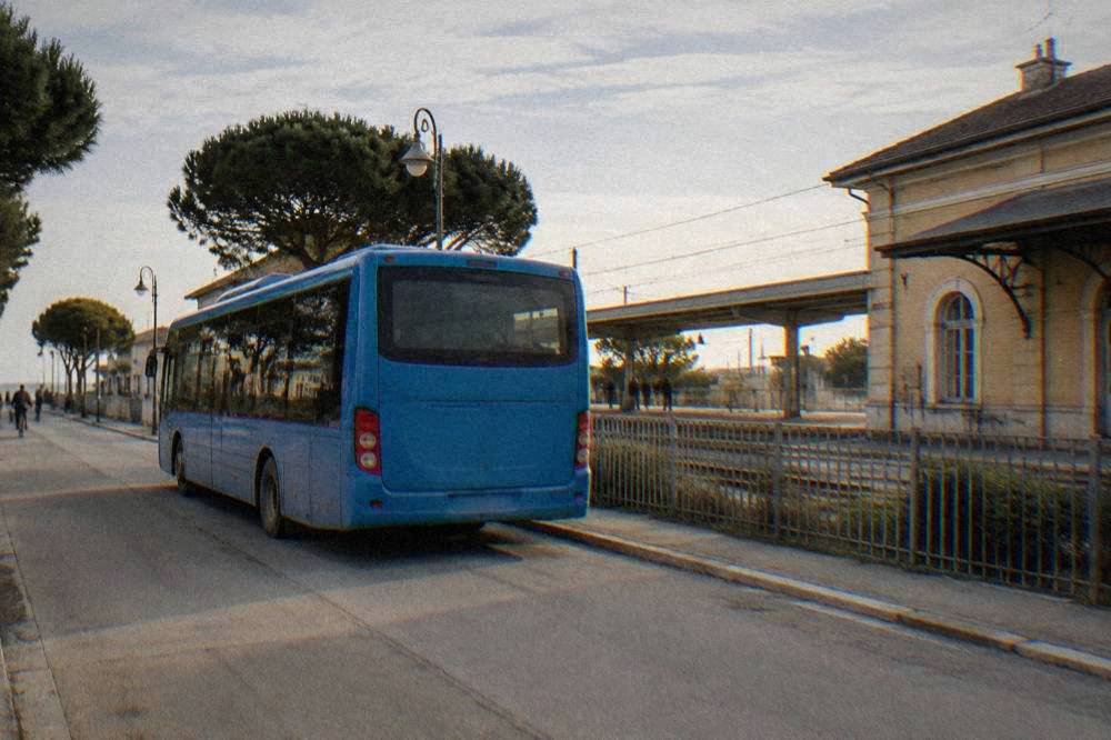 Blue regional shuttle bus parked on a quiet street beside a railway station