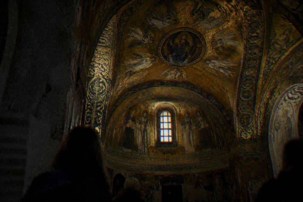 Golden Byzantine mosaic vault with figures and decorative patterns lit inside a dark chapel