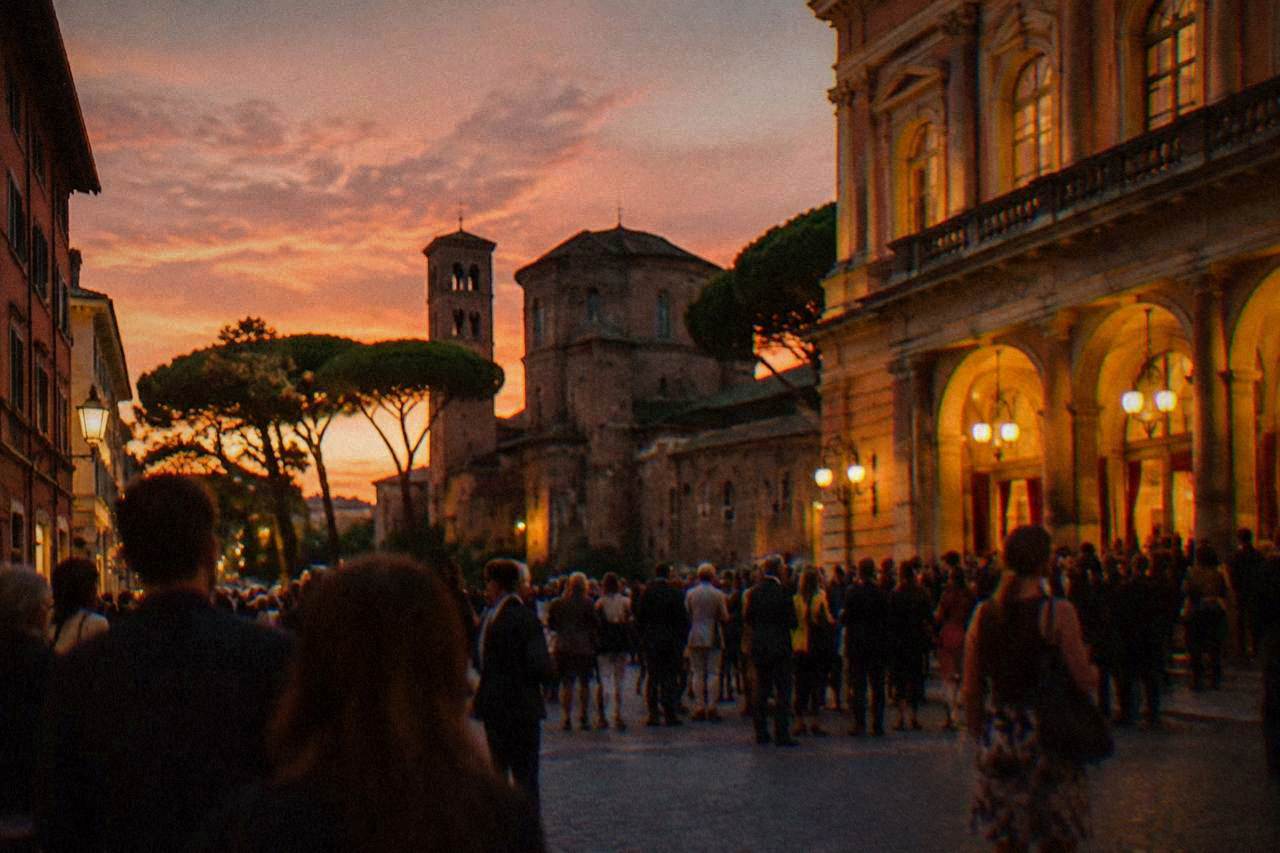 An illuminated historic square in Ravenna during an evening festival with crowds walking between stone buildings