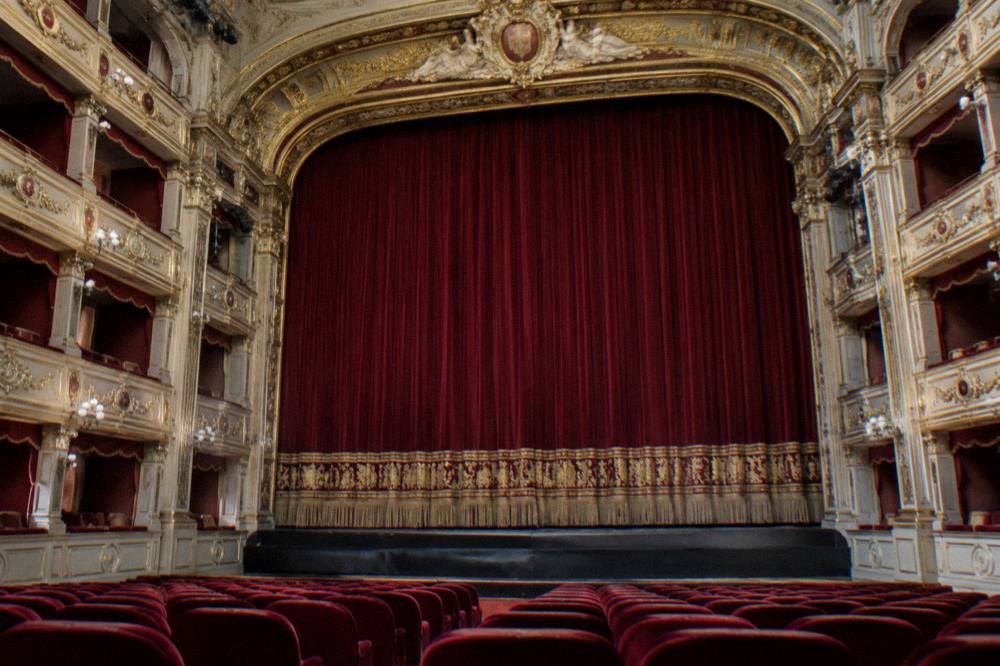The gilded proscenium arch and curtain of Teatro Alighieri seen from the stalls before a performance
