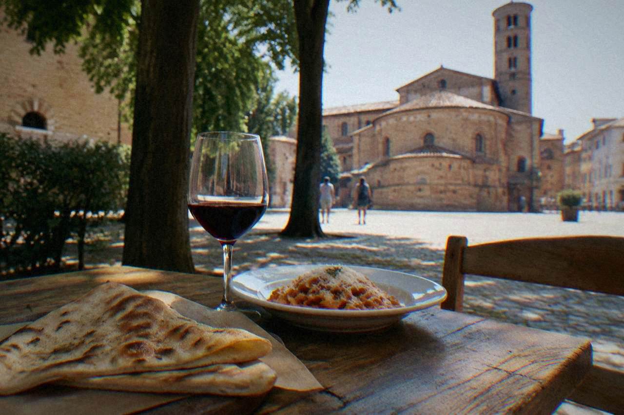 A rustic wooden table in Ravenna holding a folded flatbread, a glass of red wine and a small plate of pasta