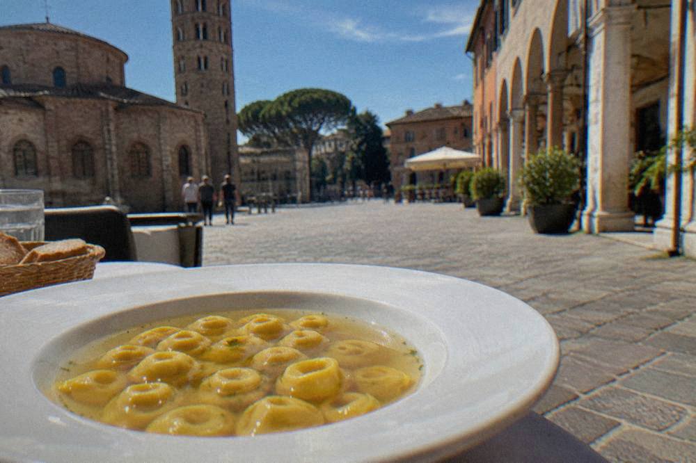 A plate of small hat-shaped filled pasta served in clear golden broth