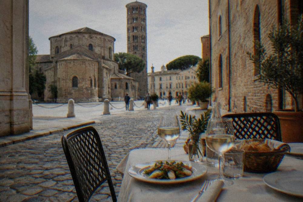 An outdoor table set for lunch on a cobbled Ravenna street near a piazza