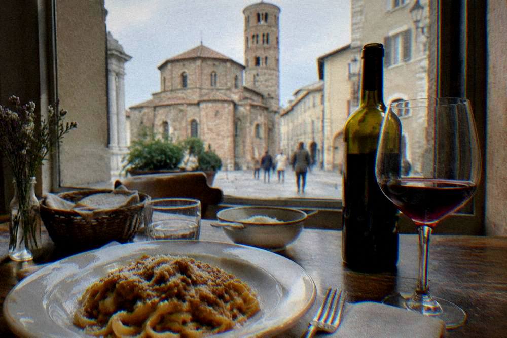 A wooden table with a homemade pasta lunch and a bottle of Romagna wine beside a window