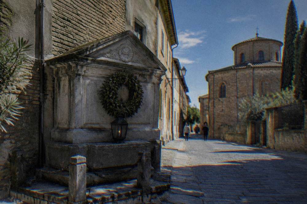 A small stone tomb with a lamp and laurel wreath in a quiet Ravenna street