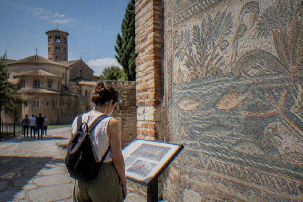 Visitor reading an information panel beside a mosaic wall in Ravenna