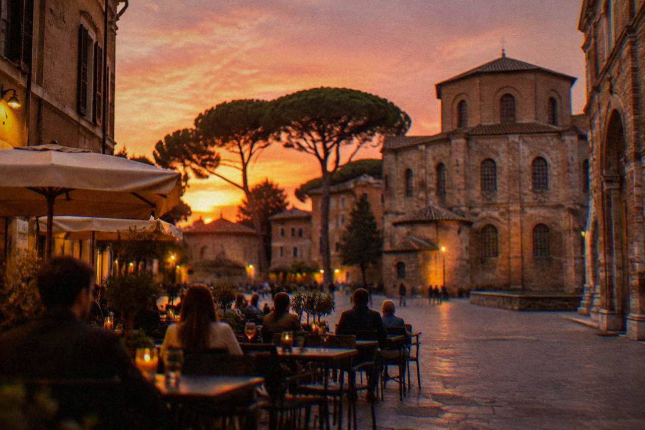 A lit piazza in Ravenna at dusk with people seated at outdoor cafe tables