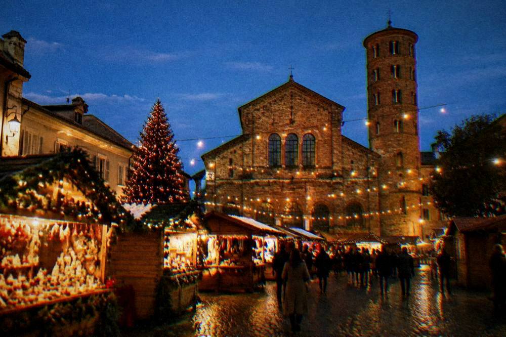 A Christmas market square with wooden stalls and string lights at night
