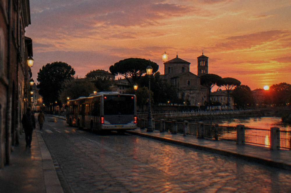 A lit waterfront street in the evening with a shuttle bus waiting
