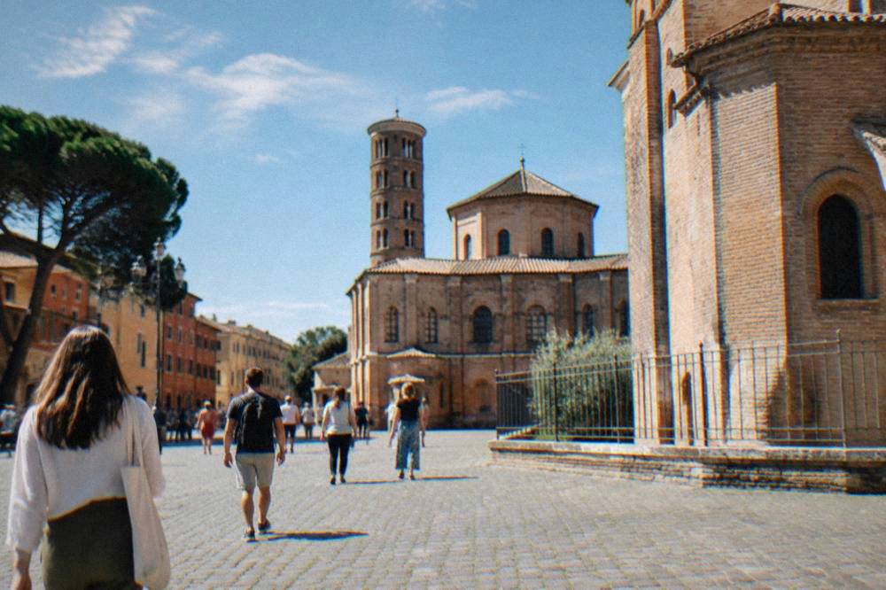 People walking across a sunlit cobbled square in Ravenna