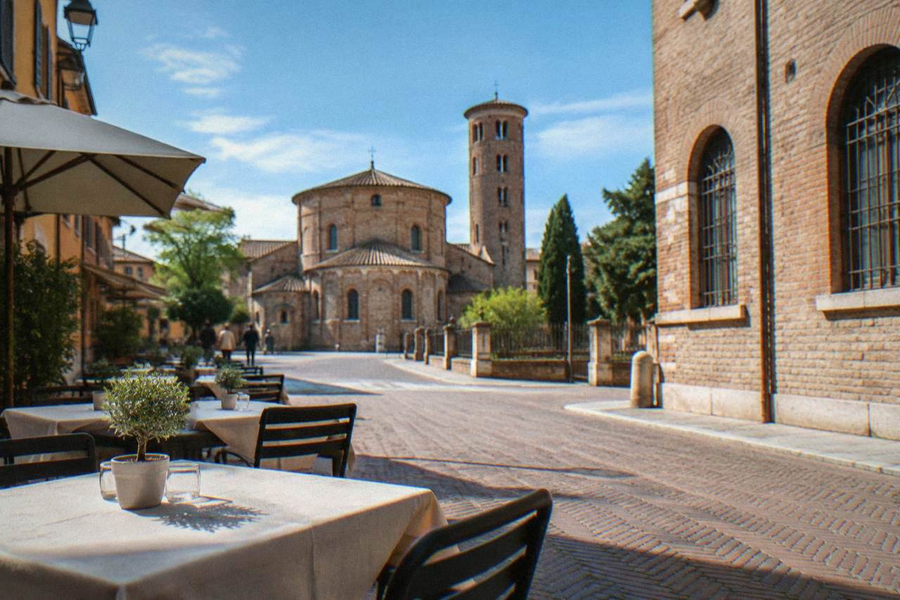 Outdoor tables of a small restaurant on a brick-paved street in a historic Italian town